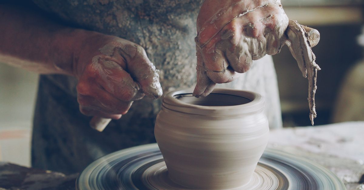 A potter shaping clay on a wheel in the studio
